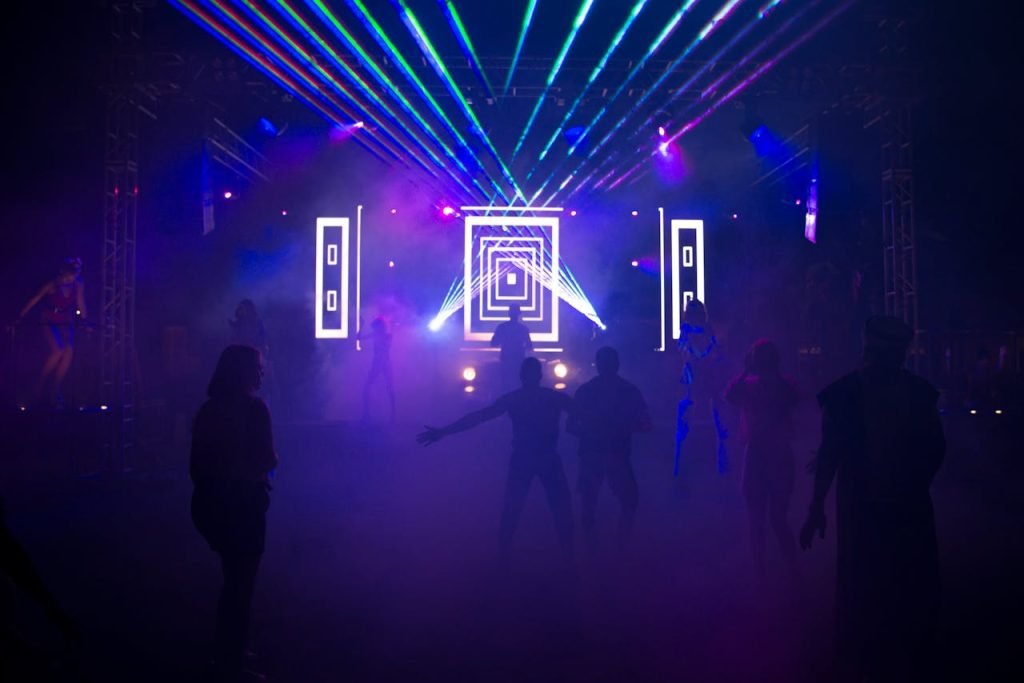 Silhouetted crowd dancing in a vibrant nightclub with colorful laser lights and smoke effects.